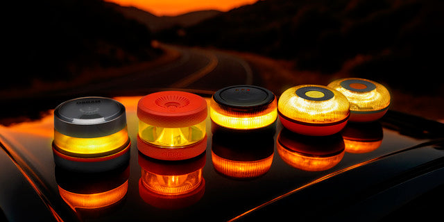 Modelos de baliza V16 conectada de Geobaliza encendidos sobre un coche al atardecer, mostrando su luz de emergencia certificada..