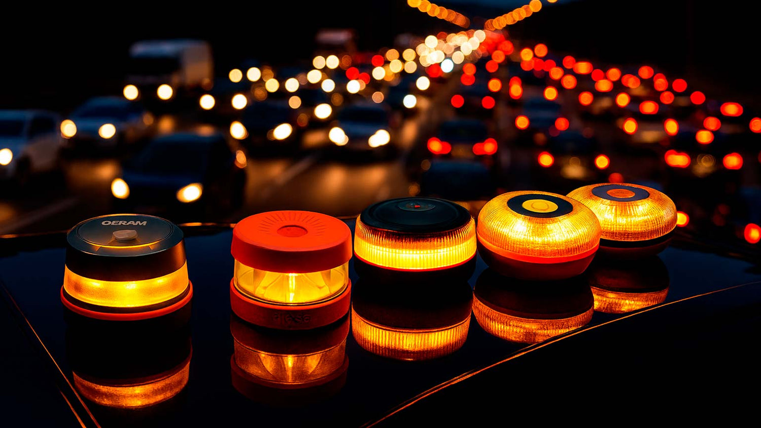 Cinco balizas V16 encendidas sobre el techo de un coche, iluminando con destellos ámbar frente a una carretera llena de coches en cola, simbolizando la alta demanda y posible escasez de stock antes de 2026.
